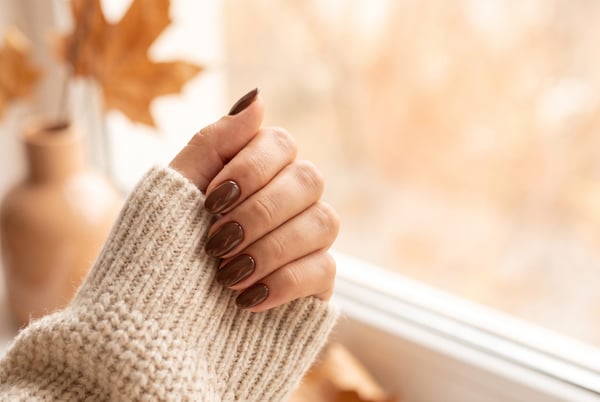 Autumn 2026 nail idea: A hand with short glossy espresso-brown almond nails resting on a cream knit jumper in warm autumn light