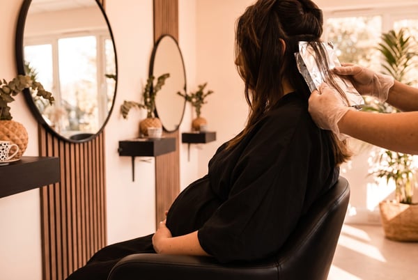 An illustration of foil highlights being applied to a pregnant client from behind, at the NU Beauty hair salon in Haverhill, with no face visible