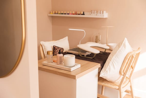 The nail studio at NU Beauty Studio in Kedington, a light-wood manicure desk with a nail lamp and a floating shelf of polishes, calm and ready for a soak-off