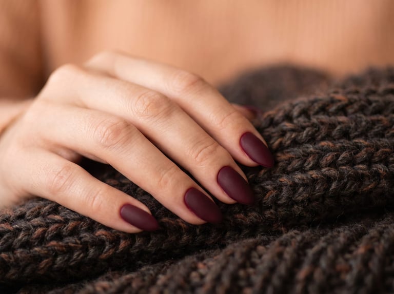 Autumn 2026 nail idea: Medium almond nails in a deep burgundy velvet matte finish resting on a dark wool scarf