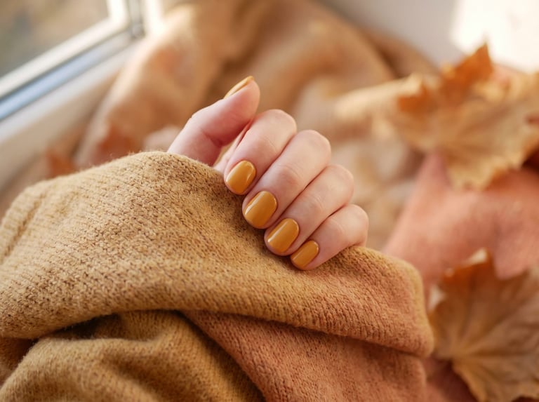 Autumn 2026 nail idea: Short rounded nails in a warm mustard ochre yellow on a mustard knit with autumn leaves