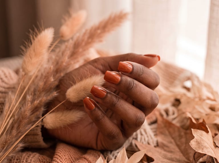 Autumn 2026 nail idea: Short square nails in a warm burnt orange resting against dried pampas and autumn leaves