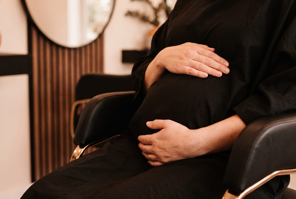 An illustration of a pregnant client resting her hands on her bump while seated in the NU Beauty hair salon in Haverhill
