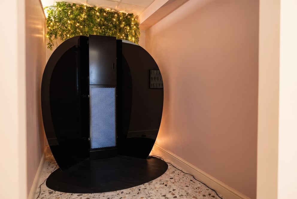 The spray tan booth at NU Beauty in Haverhill, framed by trailing greenery and warm string lights